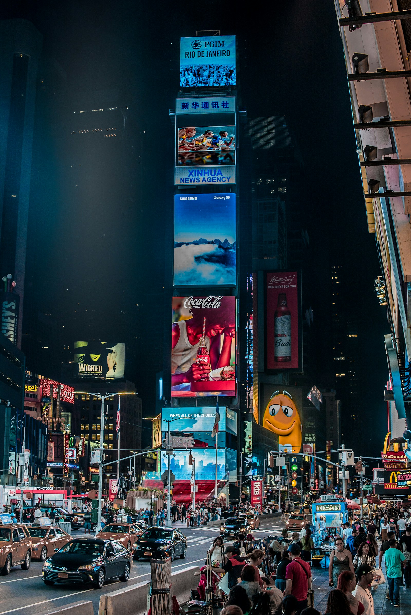 Pantallas publicitarias iluminan Times Square por la noche, entre edificios, taxis y peatones.